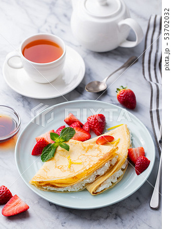 Crepes, thin pancakes with fresh strawberry and ricotta with cup of tea. Marble background. 53702032