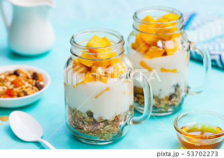 Fresh mango fruit with yogurt and granola in jars. Blue stone background. Close up. 53702273