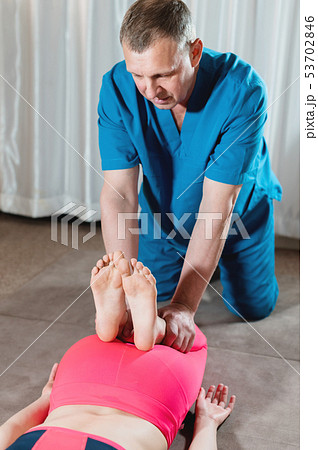 A male physiotherapist is stretching the knee joints to a young girl patient. Manual Wellness 53702846