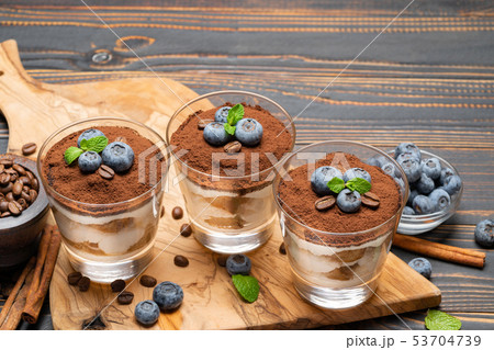 Classic tiramisu dessert in a glass with blueberries on wooden background Classic tiramisu dessert in a glass with blueberries on wooden background 53704739