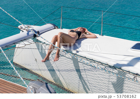 Woman relaxing on a summer sailing cruise, sitting on a luxury catamaran near picture perfect white 53708162
