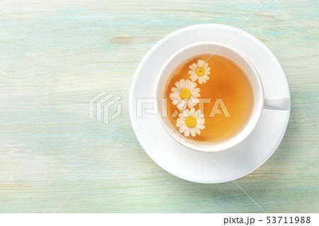 A cup of chamomile tea with steeping flowers, shot from the top on a teal blue background with a 53711988