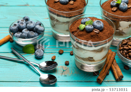 Classic tiramisu dessert in a glass with blueberries on blue wooden background Classic tiramisu dessert in a glass with blueberries on blue wooden background 53713031
