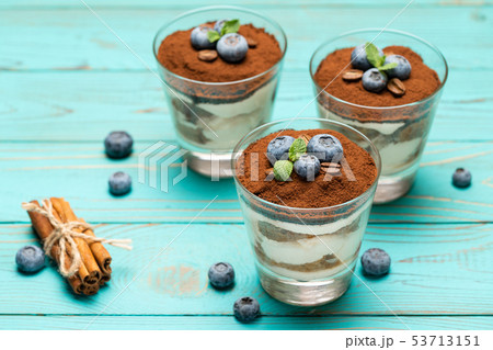 Classic tiramisu dessert in a glass with blueberries on blue wooden background Classic tiramisu dessert in a glass with blueberries on blue wooden background 53713151