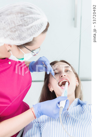 Close-up A professional dentist woman in glasses and overalls examines the oral cavity of a young Close-up A professional dentist woman in glasses and overalls examines the oral cavity of a young 53720492