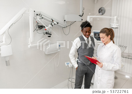 Young Woman dentist makes a diagnosis and records recommendations. African male patient in dental Young Woman dentist makes a diagnosis and records recommendations. African male patient in dental 53722761