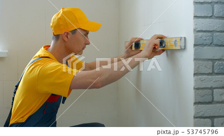 Caucasian builder measuring wall with level tool. Caucasian builder measuring wall with level tool. 53745796
