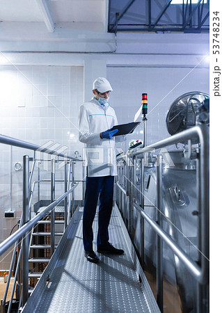 Inspector in a mask and a scrub stands with a folder-tablet in his hands at the dairy plant 53748234