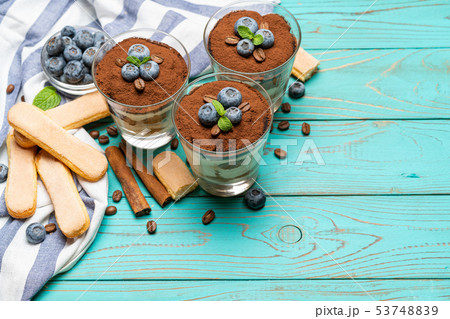 Classic tiramisu dessert in a glass with blueberries on blue wooden background Classic tiramisu dessert in a glass with blueberries on blue wooden background 53748839
