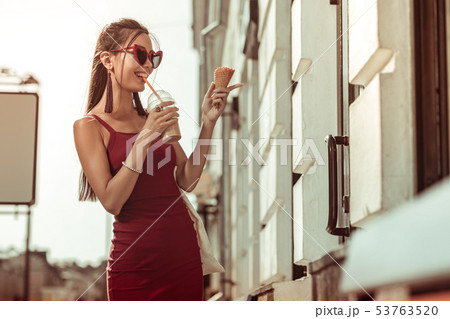 Dark-haired pleasing bewitching lady drinking ice-latte while walking the streets 53763520