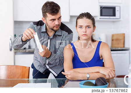 Upset young man with bill having conflict with girl in home interior Upset young man with bill having conflict with girl in home interior 53767862