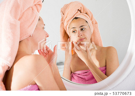 Adult woman with a towel on her head looks in the mirror Adult woman with a towel on her head looks in the mirror 53770673