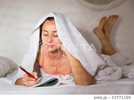 Young smiling woman writing to diary under blanket in bed 53771189
