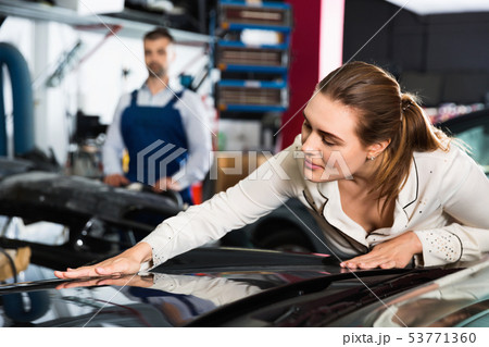 Female client closely examining car body after repainting in auto workshop 53771360