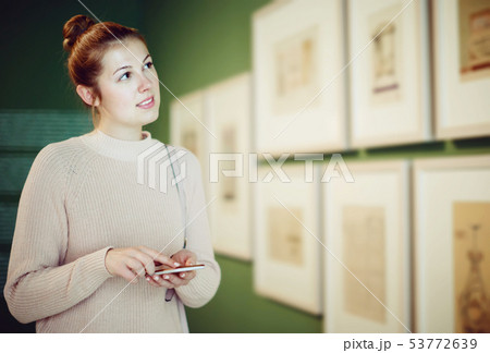 Positive woman visitor using mobile in museum Positive woman visitor using mobile in museum 53772639