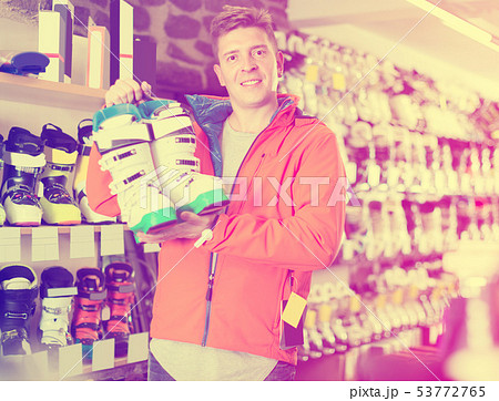 Man 22-28 years old in helmet and jacket is demonstrating ski boots 53772765