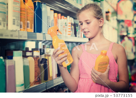 smiling teenager girl choosing bottles of sun protection indoors 53773155