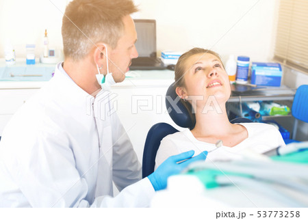 Stomatologist in uniform is taking visional inspection of a girl on the chair 53773258
