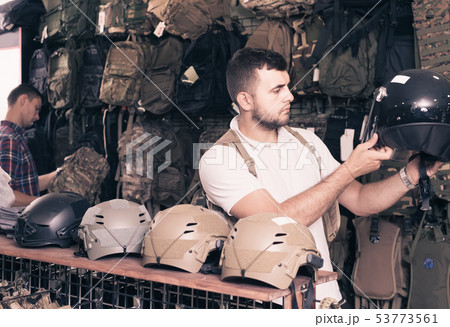Young guys choosing helmet in military shop Young guys choosing helmet in military shop 53773561