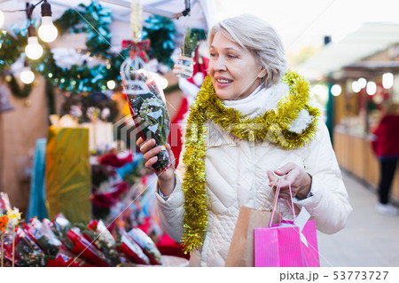 Mature female in tinsel choosing brush of Christmas tree Mature female in tinsel choosing brush of Christmas tree 53773727