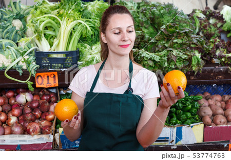 Seller female is holding oranges on her workplace in the market. Seller female is holding oranges on her workplace in the market. 53774763