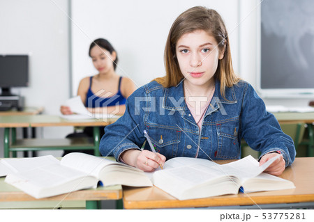 Young girl is sitting at the desk and reading text in the classroom Young girl is sitting at the desk and reading text in the classroom 53775281