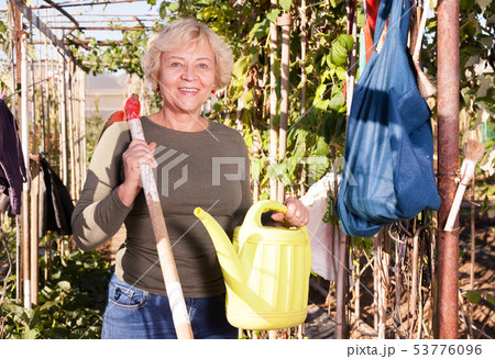 Woman posing with watering can in garden Woman posing with watering can in garden 53776096
