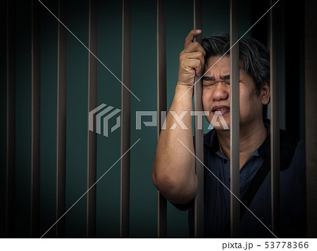 Sad asian man in prison behind bars. 53778366