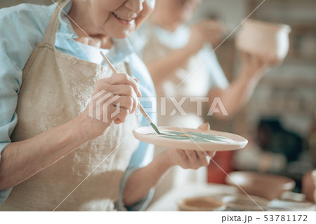 Cropped photo of elderly craftswoman painting decorative plate in workshop Cropped photo of elderly craftswoman painting decorative plate in workshop 53781172
