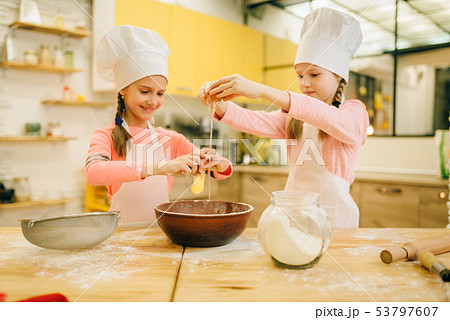 Little sisters cooks in caps kneads eggs in a bow Little sisters cooks in caps kneads eggs in a bow 53797607