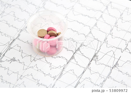 Pink and brown pills in graduated glass on EKG Pink and brown pills in graduated glass on EKG 53809972