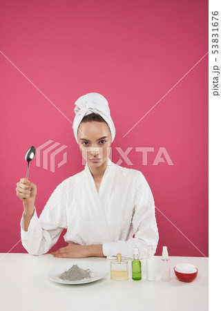 Pretty young lady in bathrobe sitting at the table with cosmetic products Pretty young lady in bathrobe sitting at the table with cosmetic products 53831676