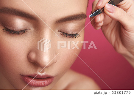 Beautician arm plucking lady eyebrows with tweezers Beautician arm plucking lady eyebrows with tweezers 53831779
