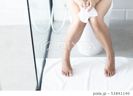 Closeup woman sitting on toilet with tissue paper Closeup woman sitting on toilet with tissue paper 53841140