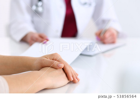 Unknown doctor woman consulting patient while filling up an application form at the desk in hospital 53856564