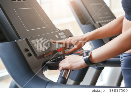 Starting to run. Close up photo of woman in sportswear pushing a start button on treadmill at gym Starting to run. Close up photo of woman in sportswear pushing a start button on treadmill at gym 53857500