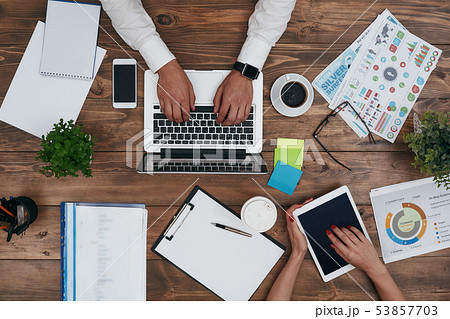 Co-workers sharing the same desk with customized workspace and working with a laptop and digital 53857703