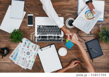Co-workers sharing the same desk with customized workspace and working with a laptop and digital 53857704