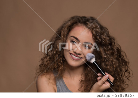 Portrait of a young woman with make-up brush in a studio against brown background. Portrait of a young woman with make-up brush in a studio against brown background. 53859257
