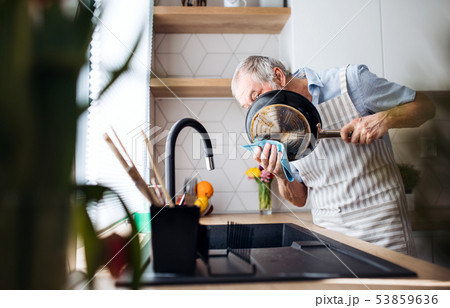 A senior man indoors in kitchen at home, washing up a pan. 53859636