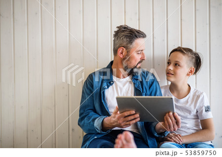 Mature father with small son sitting indoors, using tablet. Copy space. 53859750