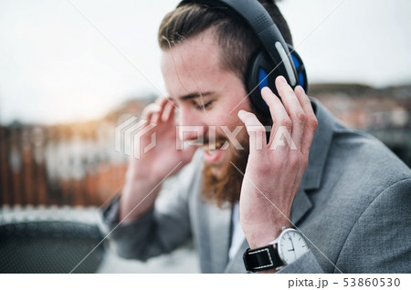 A young businessman with headphones on a terrace, listening to music. 53860530