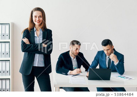 Portrait of young smiling business woman with crossed arms and her business team on background 53864484