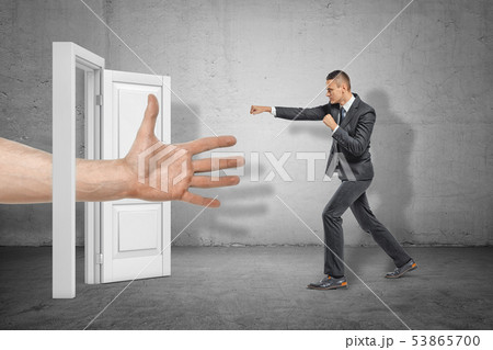 Big male open hand appearing through white doorway and businessman making kicking gesture on grey Big male open hand appearing through white doorway and businessman making kicking gesture on grey 53865700