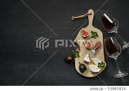 Two glasses of red wine and a tasty cheese plate on a wooden kitchen plate. Two glasses of red wine and a tasty cheese plate on a wooden kitchen plate. 53865824