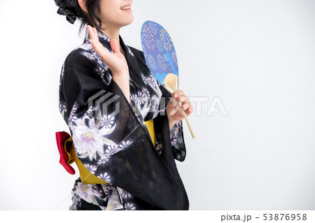 浴衣を着た30代のきれいな女性が白背景でうちわを持って待ち合わせしているの写真素材