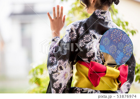 浴衣を着た30代のきれいな女性が緑の前で立って待ち合わせをして手を振っているの写真素材