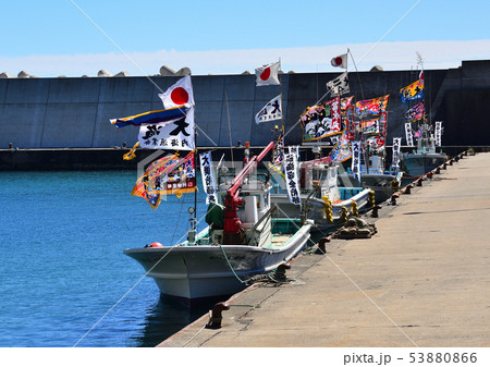 船祭りで、カラフルな大漁旗を飾り付けた数艘の漁船が漁港に一列に並んで停泊している 53880866
