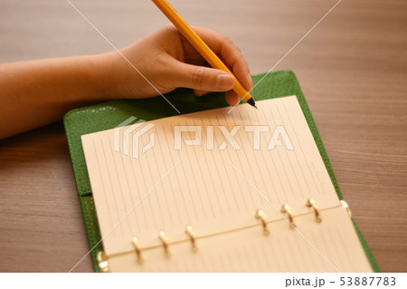 オレンジ色のボールペンで、緑色のカバーのシステム手帳に書き込むところ。② オレンジ色のボールペンで、緑色のカバーのシステム手帳に書き込むところ。② 53887783
