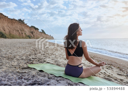 Happy young woman practices yoga and meditates in the lotus position on the beach Happy young woman practices yoga and meditates in the lotus position on the beach 53894488